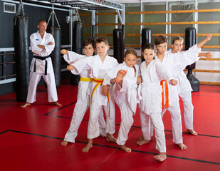 Group of emotional kids with man trainer posing in gym after taekwondo workout