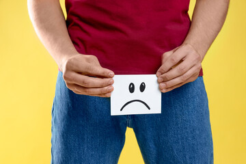 STD (sexually transmitted diseases). Man holding sticky note with drawn sad face on yellow...