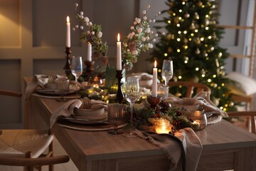 Christmas table setting with stylish dishware, glasses and burning candles in festive decorated room