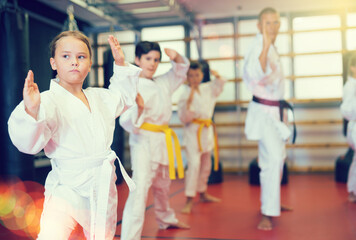 Karate kids in kimono performing kata moves with their teacher in gym during group training.