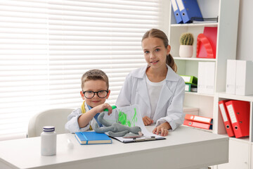 Obraz premium Little boy and girl pretending to be doctors at white table indoors