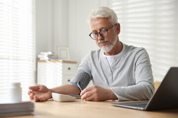 Fototapeta premium Senior man measuring blood pressure at table indoors
