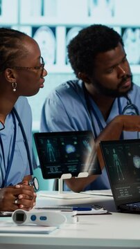 Vertical video African american general practitioner leading a healthcare team in a cabinet, analyzing MRI imaging results and providing accurate diagnosis and effective treatment. Medical facility