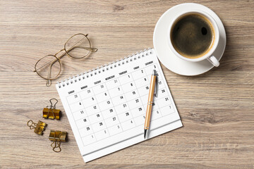 Timetable. Monthly planner, glasses, coffee, pen and clips on wooden table, flat lay