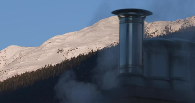 煙に覆われた煙突と雪山が見える風景。