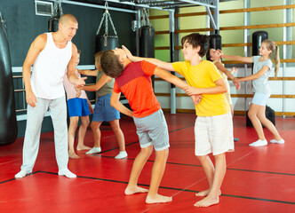 Obraz premium Kids exercising chin strike together on their self-defence training. Their teacher standing nearby and observing.