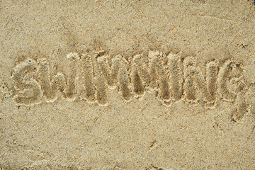 word swimming written on the beach sand