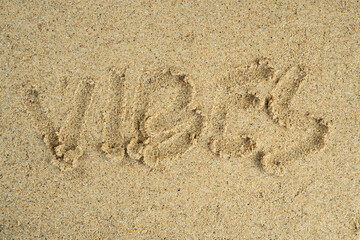word vibes written on the beach sand