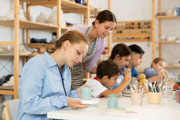 Teenage girl paints a ceramic glass made for a master class with a brush. Children make pottery at a workshop in a creative studio
