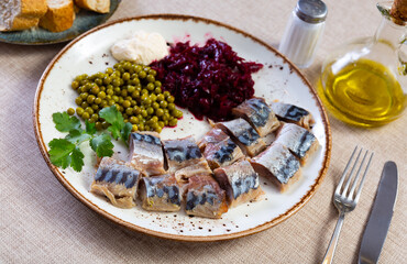 Tasty herring fish with canned green peas and beetroot cabbage on plate