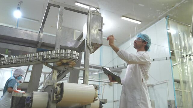 Inspector checking automated machinery in food production facility Focus on quality control safety and workflow efficiency. Worker overseeing food packaging machinery in a modern manufacturing plant.