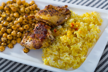 Grilled chicken thighs with garbanzo and yellow rice at plate on table