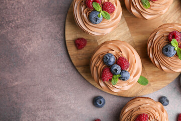 Tasty cupcakes with chocolate cream and berries on brown table, flat lay. Space for text