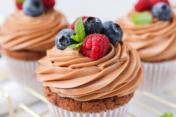 Tasty cupcakes with chocolate cream and berries on table, closeup