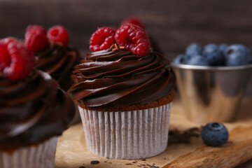 Tasty cupcakes with chocolate cream and berries on wooden board, closeup