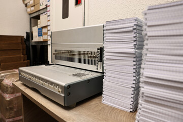 Modern binding machine and stacks of notebooks on wooden table indoors