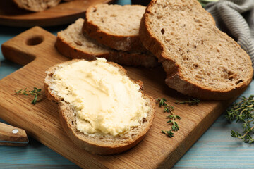 Fresh bread with butter and thyme on blue wooden table, closeup