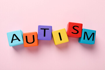 Word Autism made with colorful cubes on pink background, flat lay