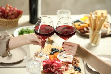 Women clinking glasses of wine during dinner at table indoors, closeup