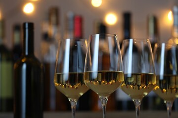 Tasty white wine in glasses against blurred background with festive lights, closeup. Bokeh effect
