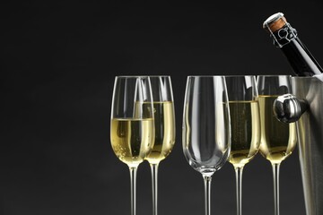 Bottle of sparkling wine in cooler bucket and glasses against grey background, closeup