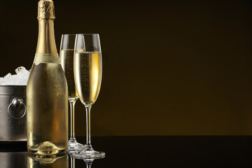 Bottle of sparkling wine, glasses and cooler bucket on black mirror surface. Space for text