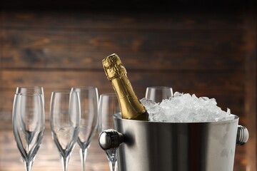 Bottle of sparkling wine in cooler bucket and glasses against wooden background, closeup © New Africa