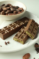Tasty Dubai chocolate bars with pistachios, knafeh and cocoa beans on light table, closeup