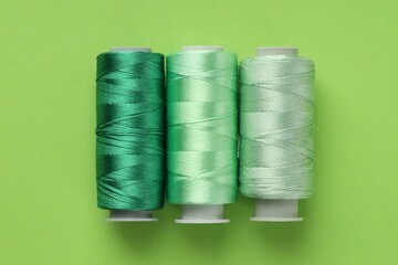 Spools of sewing threads on light green background, flat lay