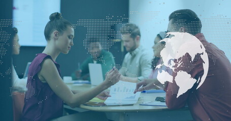 Image of world map and globe over diverse male and female colleagues at casual office meeting