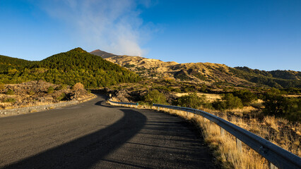 Yellow-green hills with dry grass create a stunning landscape near Mount Etna, with the majestic volcano visible in the distance. A perfect blend of natural beauty and serene Italian scenery.