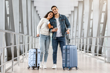 Portrait Of Cheerful Young Middle Eastern Couple Standing At Airport With Luggage And Smartphone,...