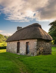 Fototapeta premium Rustic stone cottage with thatched roof basks in the golden hour light.