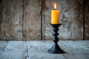 A lit yellow candle sits in a black candlestick on a rustic wooden table.