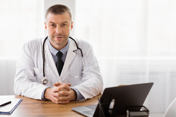 Fototapeta premium Healthcare And Medicine Concept. Portrait of mature clinician sitting at desk with laptop looking at camera