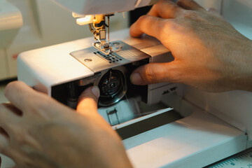 Close-up of hands threading a sewing machine bobbin, preparing the machine for sewing.