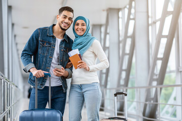 Portrait Of Happy Young Islamic Couple Standing At Airport With Luggage And Smartphone, Handsome Arab Man And Woman In Hijab Enjoying Travelling Together, Ready For Vacation Trip, Copy Space