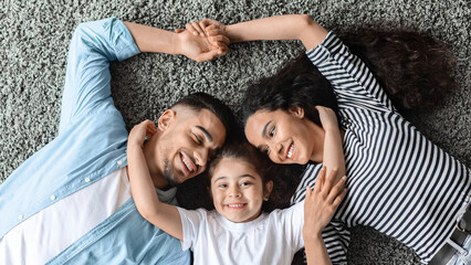 Portrait of happy middle eastern family posing on floor at home, laying on carpet and bonding,...