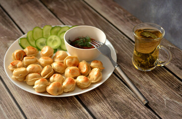 Plate with fried dumplings, tomato sauce and slices of fresh cucumber on a wooden table.