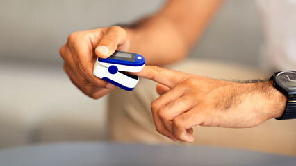 Unrecognizable man using modern pulse oximeter, closeup photo, copy space. Cropped of male patient putting clip-like small device for blood oxygen, saturation measuring and coronavirus