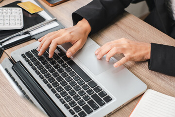 Close-up of hands typing on a laptop keyboard, surrounded by office supplies on a wooden desk.