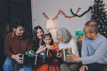 Portrait of Asian family exchanging presents during christmas at home. Attractive happy people holding gift box, celebrate holiday thanksgiving, xmas eve tradition in living room in house together.