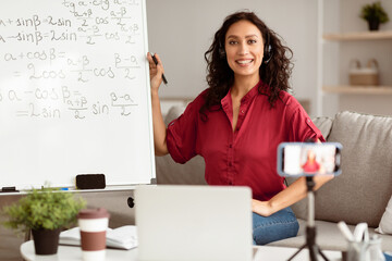 Online Learning Concept. Portrait of smiling lady teacher in headset sitting near whiteboard,...