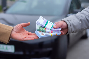 Close-up photo of hands exchanging money in front of a electric car, symbolizing a car buying and selling transaction.