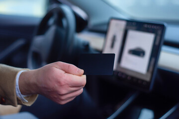 Close-up photo of a hand gripping a electric car's steering wheel with a tablet inside the cabin.
