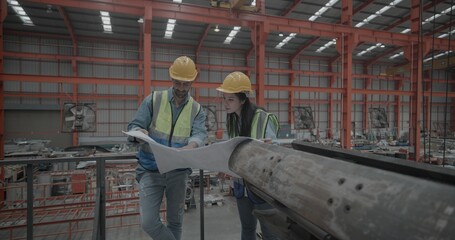 Metal sheet workers inspecting blueprint in factory setting. Collaborating on project planning and precision engineering, surrounded by machinery and equipment essential for manufacturing process.
