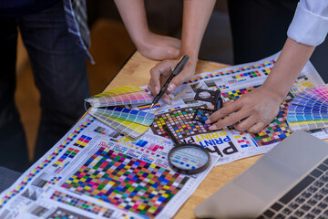 Team graphic designer checking print quality of media graphics proof print and color guides in...