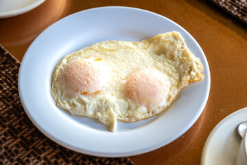 Side view of white plate with two fried eggs on the table. Food concept.