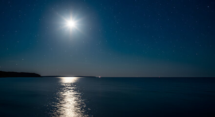 An enchanting and scenic landscape showcasing a full moon reflecting on the ocean during the night.