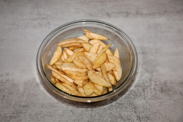 A glass bowl with sliced pear mixed with sugar and cinnamon for making pear cobbler or bread pudding.